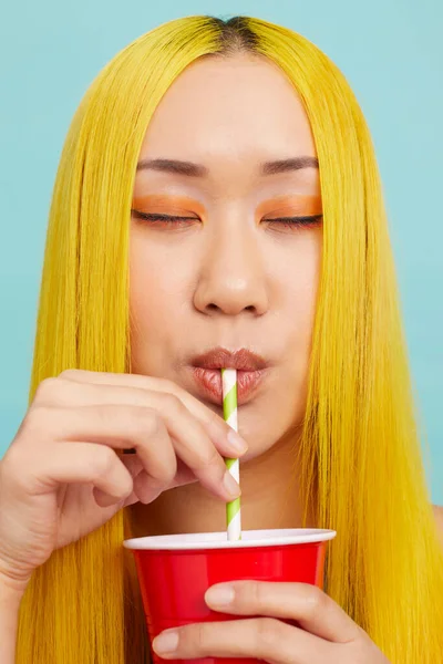 Uzun sarı saçlı, gözleri kapalı, samandan su içen genç bir kadın.