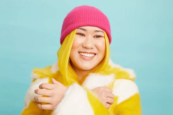 Uzun sarı saçlı, kürk manto ve pembe örgü şapkalı, gülümseyen kadın.