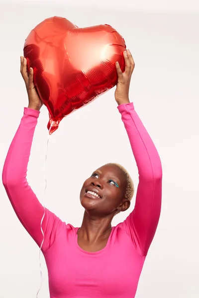 Kısa beyaz saçlı, kalp şeklinde balon tutan bir kadın. 