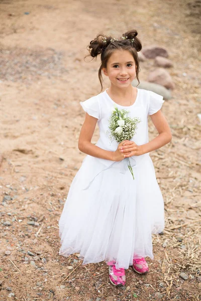 Uma criança menina detém um buquê de flores brancas em rosa sneakers.dark cabelo, flores brancas em suas mãos, vestido branco Imagens De Bancos De Imagens Sem Royalties