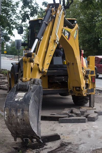 The bucket of a construction excavator breaks up the asphalt and removes building blocks — Stock Photo, Image