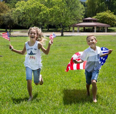 Adorable little girl and boy run on bright green grass holding american flag outdoors on beautiful summer day clipart