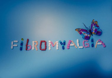  The word Fibromyalgia written by colorful medicines, pills, drugs, tablets, capsules, with purple butterfly on a blue background clipart