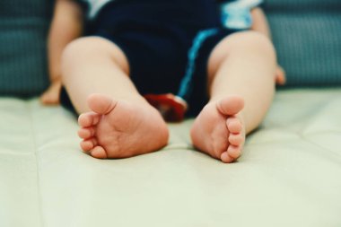 Bebek oğlan bir koltukta oturuyor Ayaklarını gösteriyor.