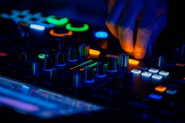 DJ elleri gece konsolda renkli kulüp ışıklarıyla karışıyor. Parti hayatı, gençler eğleniyor.