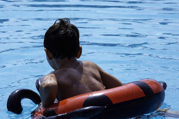 Мальчик плавает в бассейне со своим кольцом для пончиков. Семейные праздники, показывающие, как маленький мальчик развлекается в бассейне.