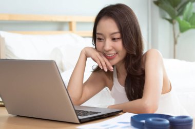 Evde yatağın üzerinde dizüstü bilgisayarda çalışan Asyalı bir kadın..