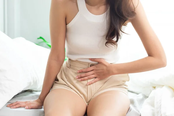 迷人的亚洲女人坐在床上会感到膀胱疼痛 — 图库照片