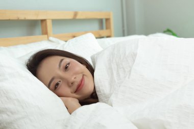 Asyalı kadınlar mutlu uyanır ve yatak odasındaki beyaz yatakta gülümser..