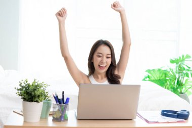 Evde yatağın üzerinde dizüstü bilgisayarda çalışan Asyalı bir kadın..