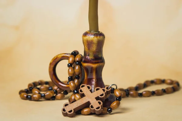 Religion concept. Christian religion. A wooden cross on a wooden chain lies next to a candlestick. Photo on a background of old paper.