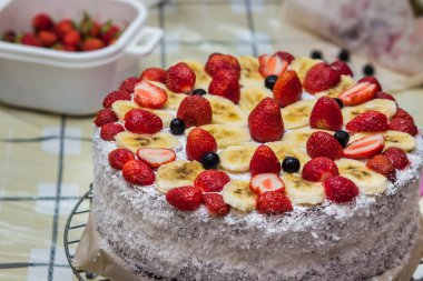 Kremalı ev yapımı meyveli pasta. Çilek ve muzla süslenmiş pasta. Yanlara hindistan cevizi serpiştirilmiş.