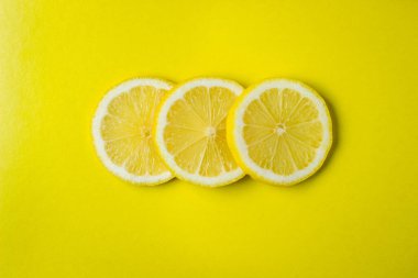 Sarı arka planda üç dilim limon üst üste yatar. Yuvarlak limon dilimleri. Fotoğraf yukarıda.