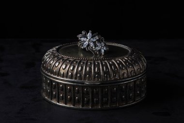 Gümüş bir yüzük gümüş bir kutunun üzerinde duruyor. Çiçek şeklinde gümüş bir yüzük. Antika gümüş kutu. Siyah arkaplanda fotoğraf