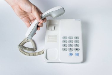 Sabit bir telefondan bir el telefonu açar. Düğmeleri olan beyaz sabit hat telefonu. Beyaz arkaplanda fotoğraf