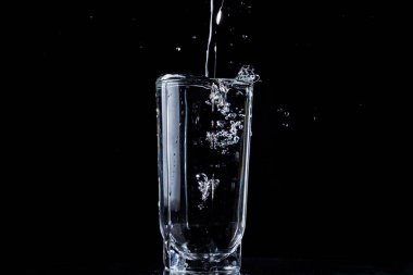 Bir su akıntısı bir bardak suya dökülür. Su bardağı taşırdı. Siyah arkaplandaki fotoğraf. Bir bardaktan dökülen saf ve saf su.