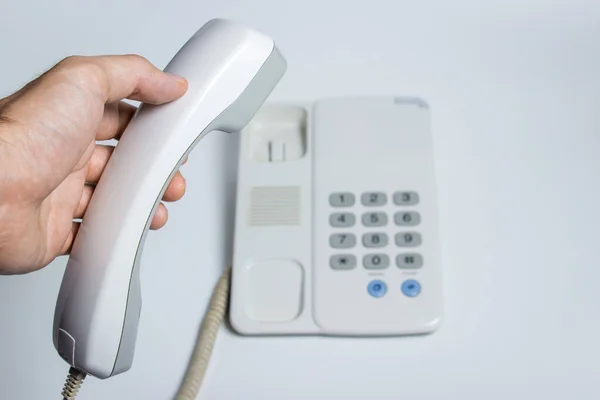 携帯電話は固定電話からの電話受信機を持っています ボタン付きの白い固定電話 白い背景の写真 — ストック写真