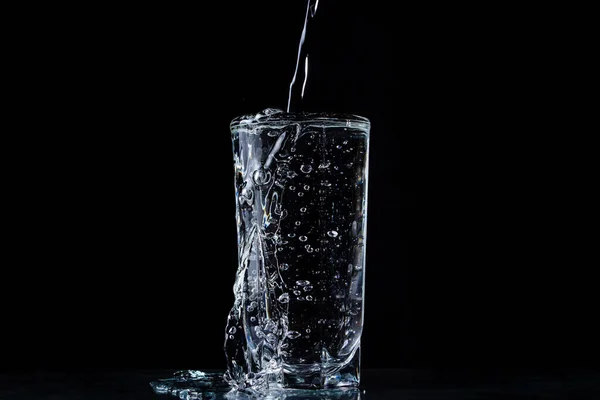 水がガラスにあふれている 黒い背景の写真 純粋で清らかな水 ガラスから水が噴き出す — ストック写真