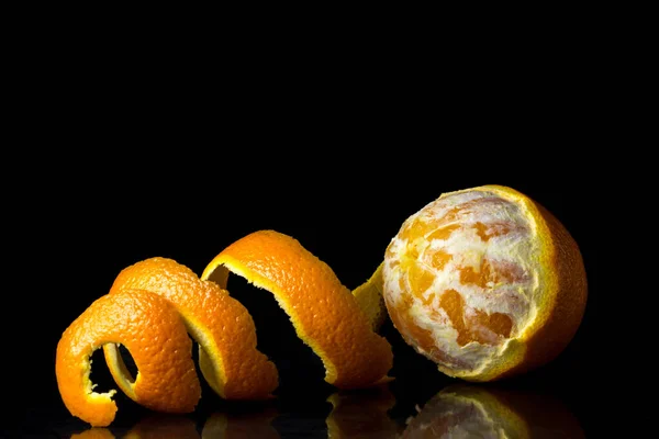 Siyah arka planda yarı soyulmuş turuncu. Kabuk yakınlarda duruyor. Tropik meyve.