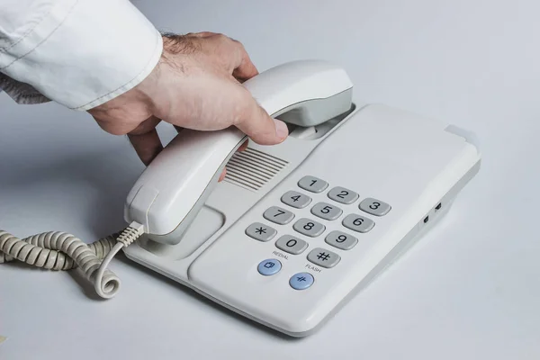 A male hand picks up the phone. Landline phone on a white background.