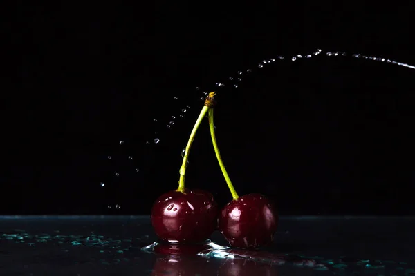 Cherry on a black background. Two cherries stand on the water. A stream of water over a cherry.