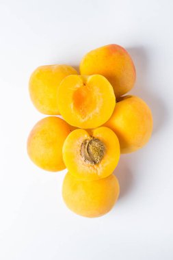 Beyaz arka planda kayısılar. Kayısıların üzerinde iki dilim kayısı var. Bir lobule kemikli, diğeri kemiksiz..