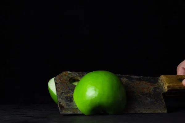 Green apple on a black background. kitchen hatchet chopping an apple in half. Hatchet old with rust