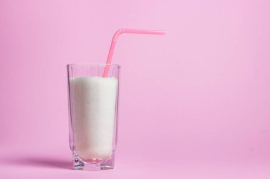 Pembe arka planda bir bardak dolusu şeker. Şekerli bir bardakta Pembe bir kokteyl kamışında