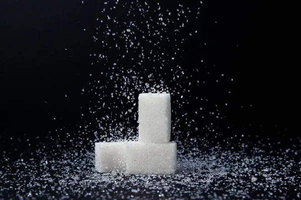 Sugar cubes on a black background. Sugar sprinkles on top. Sugar abuse concept