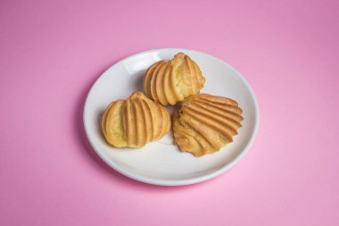 Pembe arka planda kremalı pasta. Beyaz bir porselen tabakta üç kek var.