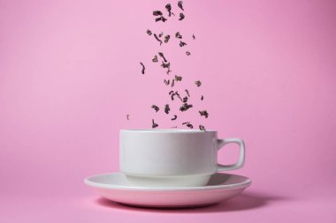 Çay yaprakları pembe arka planda beyaz bir porselen bardağa dökülüyor. Çay reklamı..