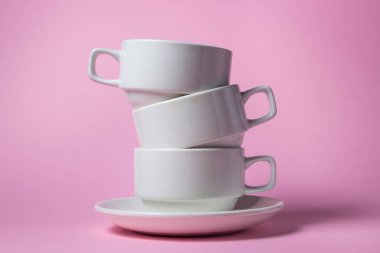 Pembe arka planda üst üste yığılmış beyaz bardaklar. Bir fincan üzerinde üç beyaz porselen bardak.