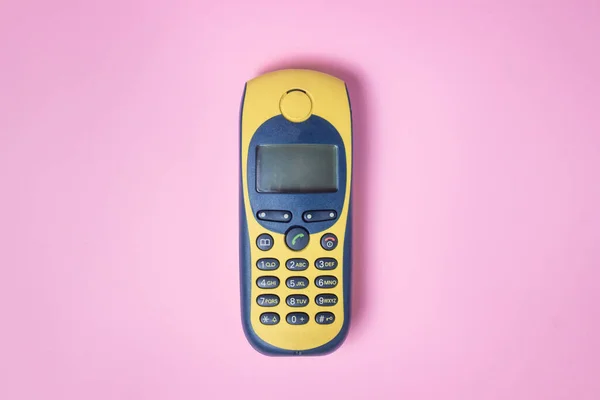 Old generation mobile phone on a pink background. Yellow and blue retro style mobile phone.