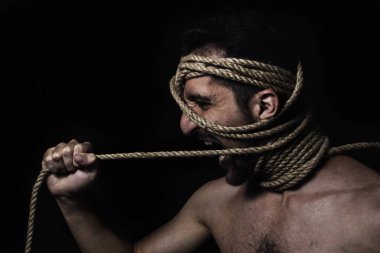 Adamın yüzü ipe sarılmış. El ipi çeker, düğümü sıkarak. Adam bağırıyor. Bir adamın yaratıcı portresi.
