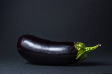 Siyah arka planda patlıcan. Çerçevenin ortasında taze bir patlıcan var..