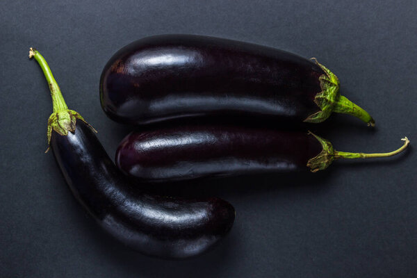 Eggplant on a black background. Several fresh eggplants lie in the middle of the frame. Photo from above