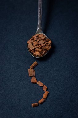 Siyah arka planda tarçın. Bir kaşık dolusu ezilmiş tarçın. Kaşığın yanında tarçın parçalarından oluşan bir patika var.