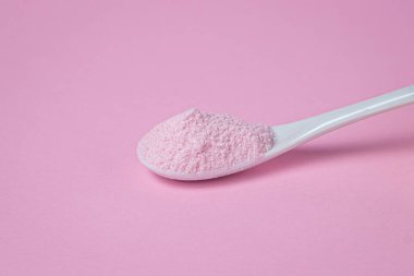 Pembe arka planda pembe tozlu bir kaşık. Vişne aromalı pembe renkli jelatinli tatlı karışımı..
