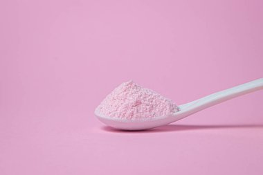 Pembe arka planda pembe tozlu bir kaşık. Vişne aromalı pembe renkli jelatinli tatlı karışımı..