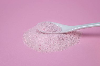 Pembe arka planda pembe tozlu bir kaşık. Kaşık pembe toz yığınının üzerinde yatıyor. Vişne aromalı pembe renkli jelatinli tatlı karışımı..