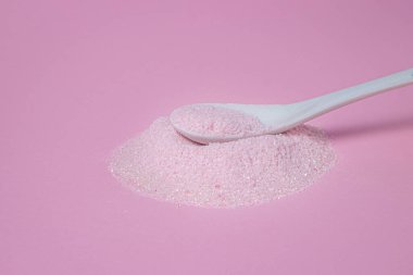 Pembe arka planda pembe tozlu bir kaşık. Kaşık pembe toz yığınının üzerinde yatıyor. Vişne aromalı pembe renkli jelatinli tatlı karışımı..