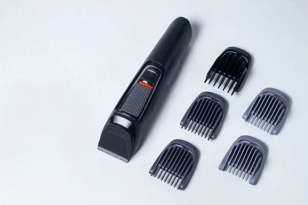 Beard trimmer on a white background. Different sized attachments are placed next to the trimmer. Beard care. Male style