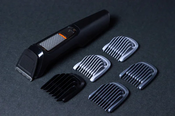 Beard trimmer on a black background. Different sized attachments are placed next to the trimer. Beard care. Male style