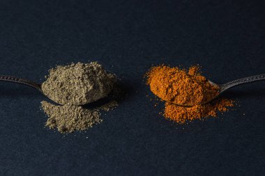 Siyah arka planda kırmızı ve kara biber. Siyah biberli kaşık kırmızı biberli kaşığın yanında yatıyor. Baharatlı biber..