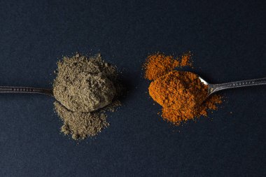 Siyah arka planda kırmızı ve kara biber. Siyah biberli kaşık kırmızı biberli kaşığın yanında yatıyor. Baharatlı biber..