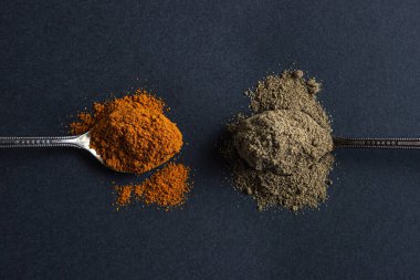 Siyah arka planda kırmızı ve kara biber. Siyah biberli kaşık kırmızı biberli kaşığın yanında yatıyor. Baharatlı biber..