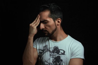 Baş ağrısı. Adam acı içinde elini tutarak başını tutuyor. Ahlaki yorgunluk. Fotoğraf siyah arkaplanda