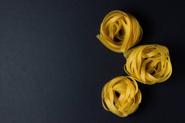 Siyah arka planda makarna yuvaları. İtalyan makarnası. Çerçevenin sağ tarafında üç makarna yuvası var. Solda bir yazı veya logo için bir yer var. Avrupa mutfağı