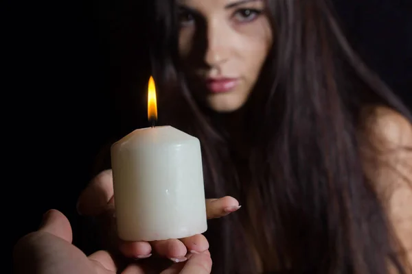 拿着燃烧的蜡烛的女孩黑色背景上的一个黑发女人把一支白色的蜡烛递给另一个人 神秘主义和算命黑魔法 — 图库照片