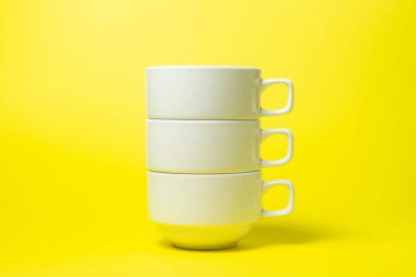 Sarı arka planda beyaz bardaklar. Üç beyaz bardak üst üste geldi. Çay takımı..